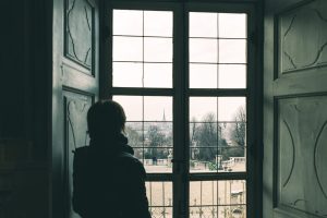 Woman looking through window, toned image, vintage style. Turin cityscape, Torino, Italy, old house, rear view in shade.
